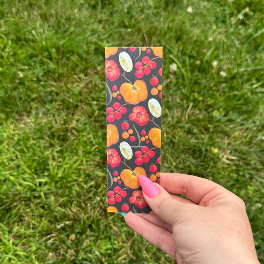 Hand holding a colorful bookmark with tomato design against a grass background