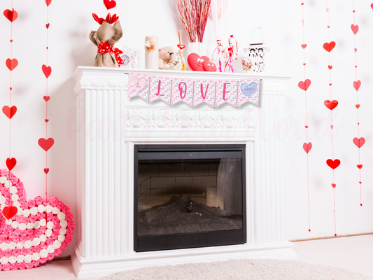 Valentine's Day fireplace decor featuring a white mantle with a 'LOVE' banner. Pink and blue candy heart designs spell the word and are surrounded by red heart garlands, plush heart shapes, and floral decor. The banner is part of a Party Your World printable DIY set