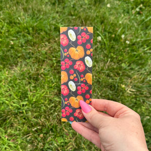 Hand holding a colorful bookmark with tomato design against a grass background