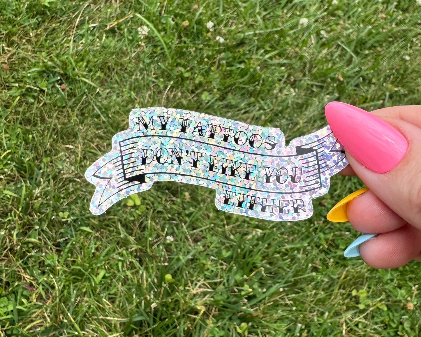 Holographic sticker with text held by a hand against a grass background