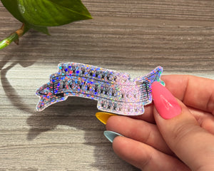 Hand holding a colorful, glittery sticker "my tattoos don't like you either" on a wooden surface