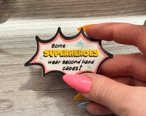 Hand holding a colorful superhero-themed sign on a wooden surface