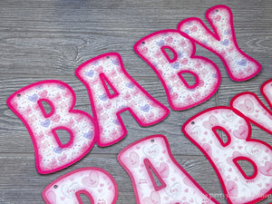 Welcome baby girl banner with pink and purple conversation heart pattern letters, adorned with hearts. A joyful celebration of a new arrival.