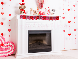 Valentine’s Day banner displayed on a fireplace mantle with heart-themed decor. The banner alternates between red and pink flags with black floral 'X,' 'O,' and heart designs.