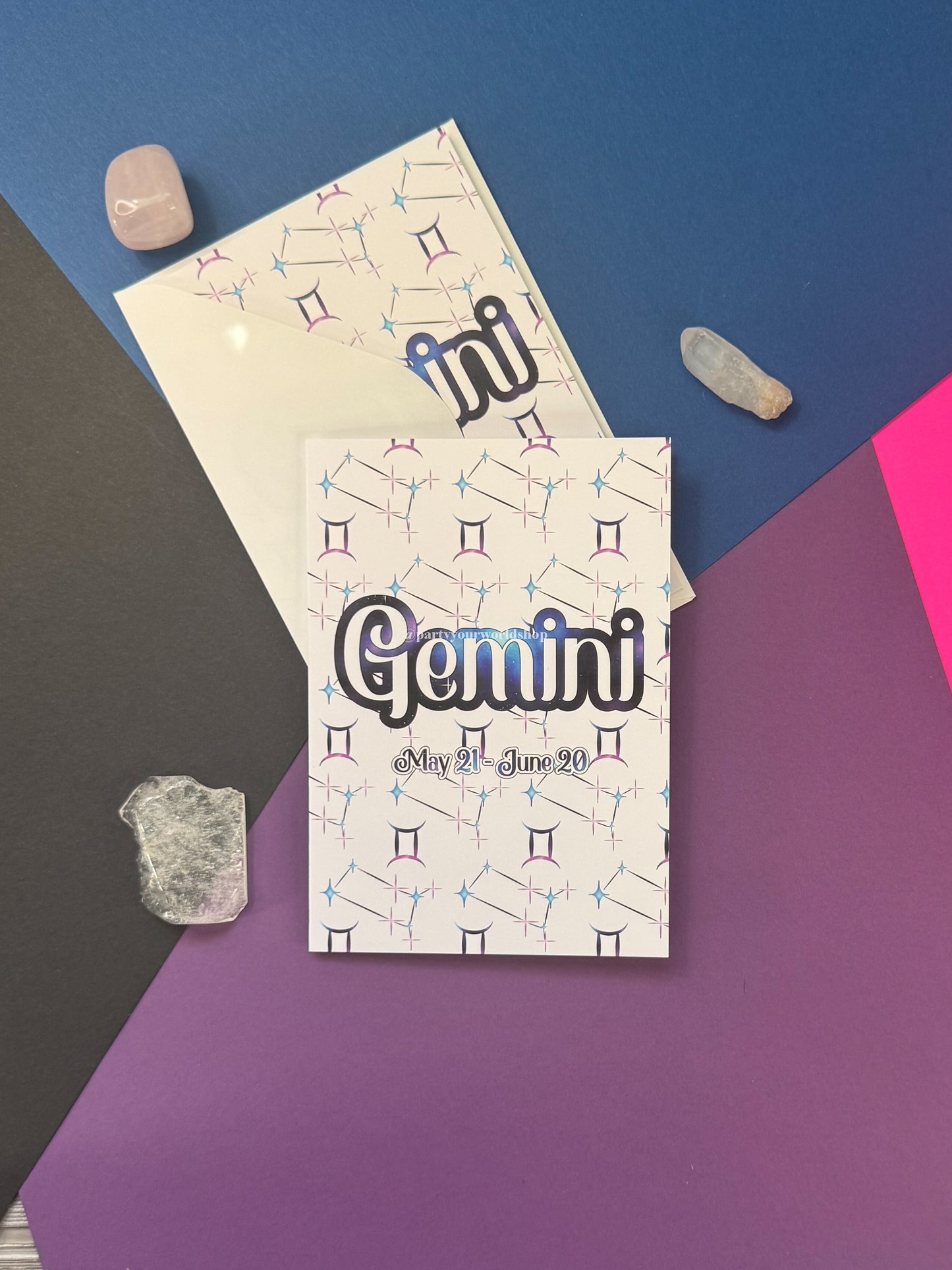 A Gemini-themed card or print featuring the word Gemini in large outlined letters with a blue gradient glow, plus the date May 21 - Jun 29, shown on a purple and blue geometric background with crystals and a second card behind it.